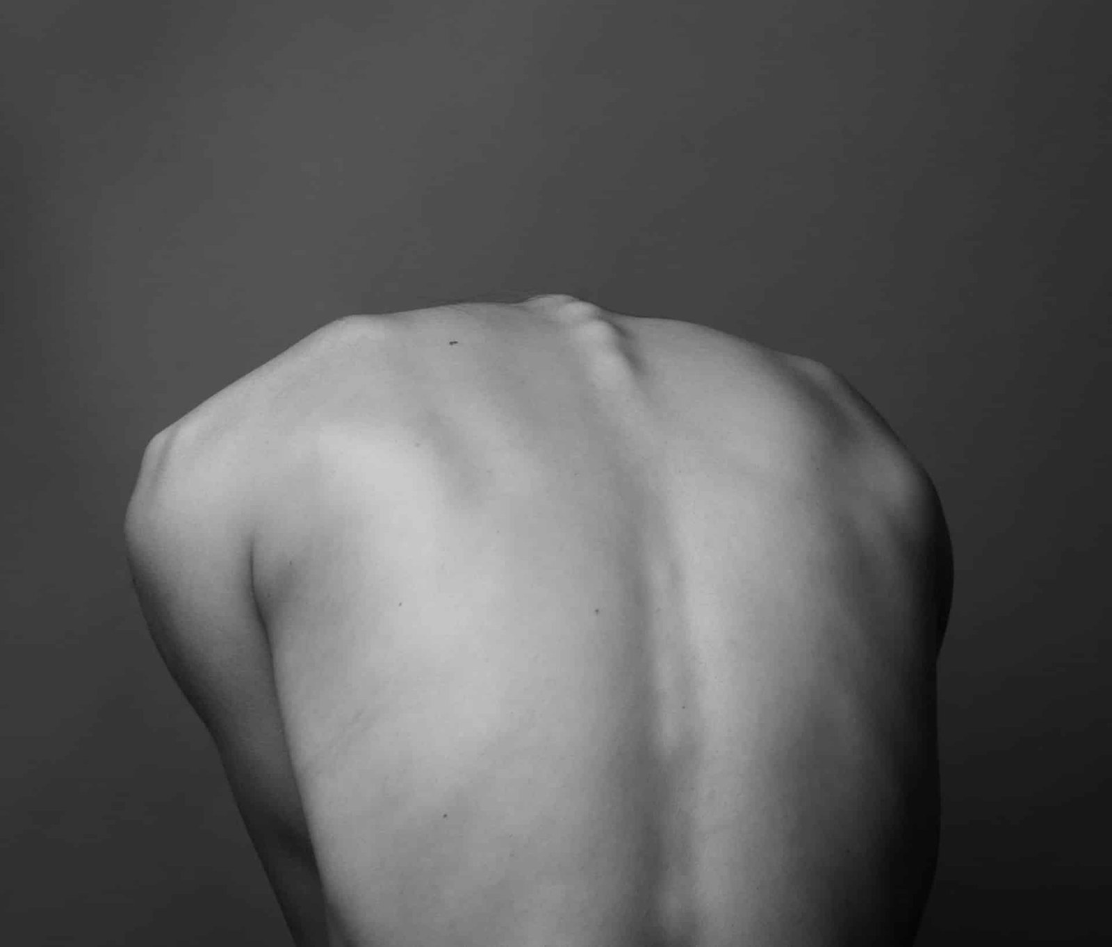 black and white photo of a human back with their head bent forward and the spine sticking out